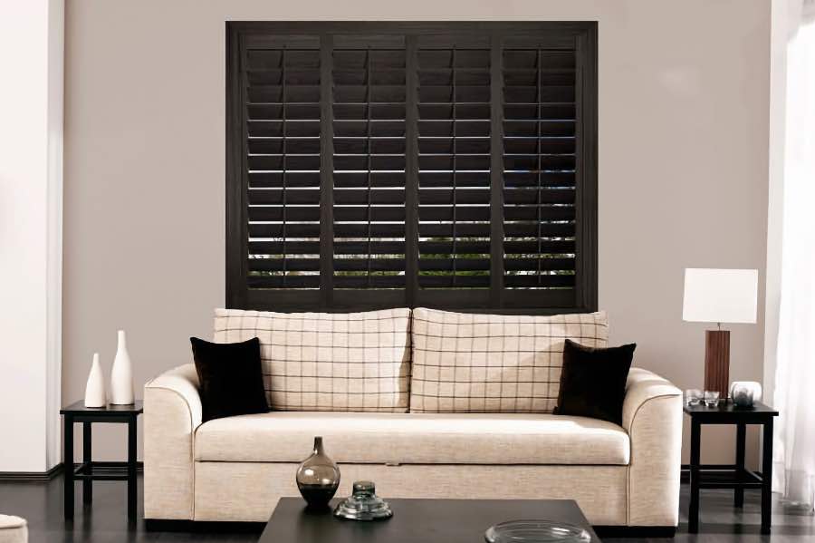 Dark wood plantation shutters on a window above a beige couch